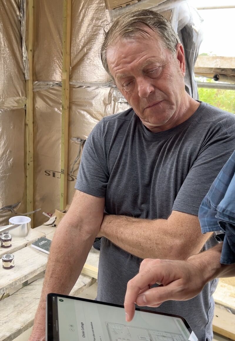 A tradesperson on site pointing at a Reno floor plan on a tablet